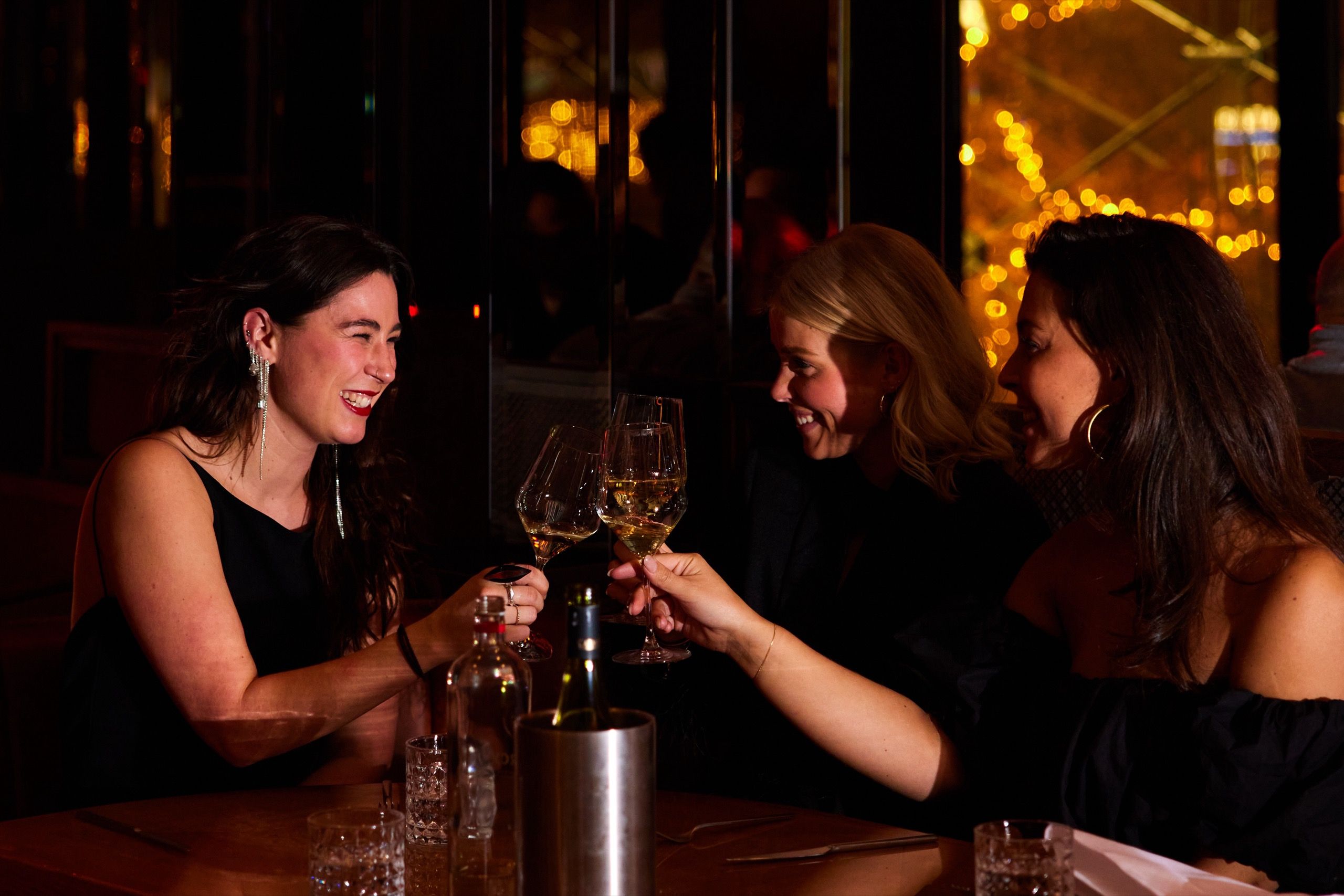 Three friends toasting with white wine at a table on the first floor