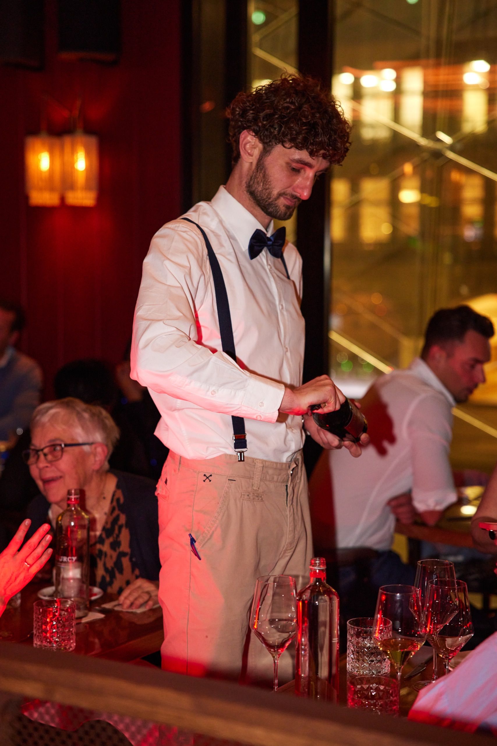 A waiter in braces pouring wine for a table of guests