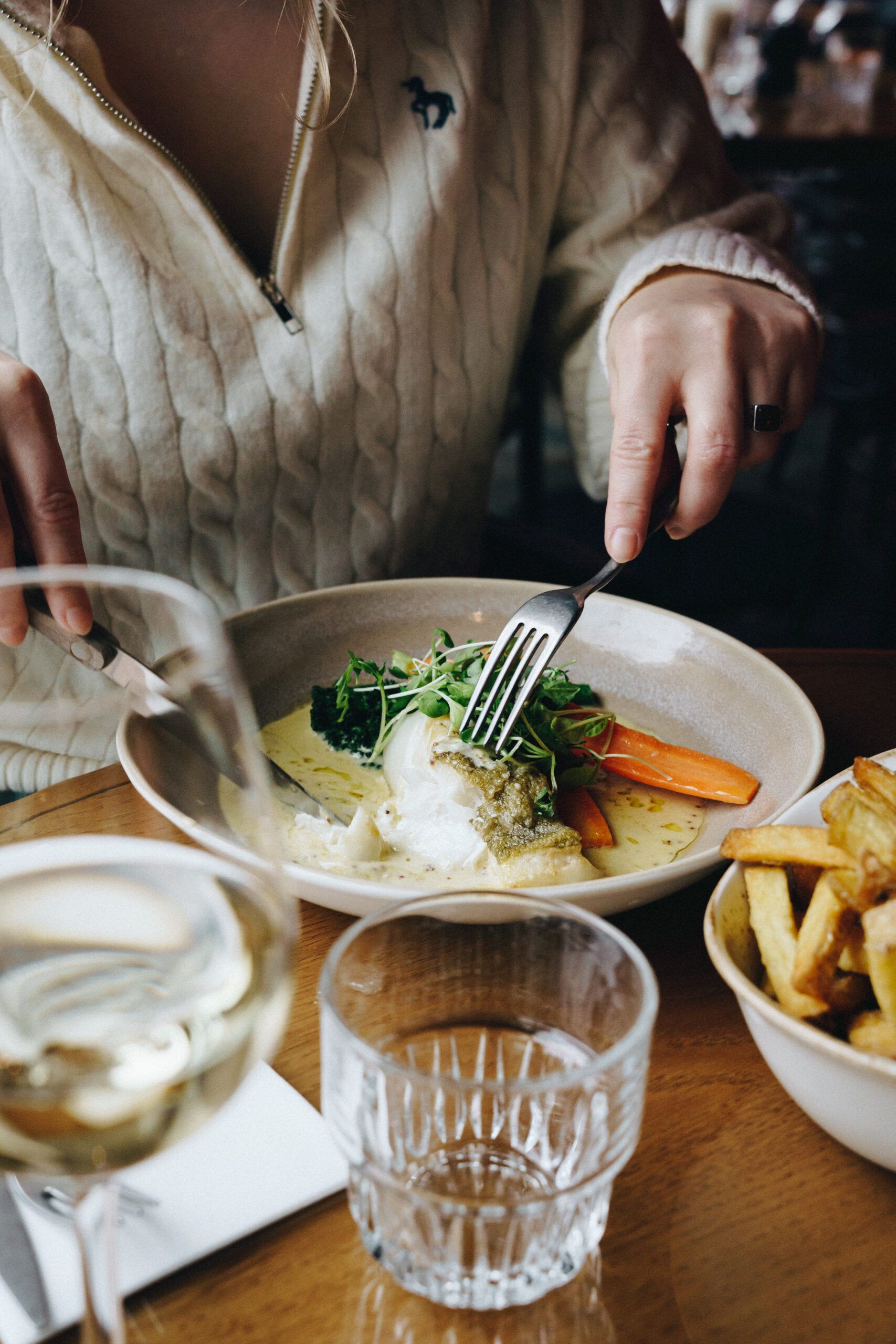 A guest eating a main course with a bowl of fries and a glass of white wine