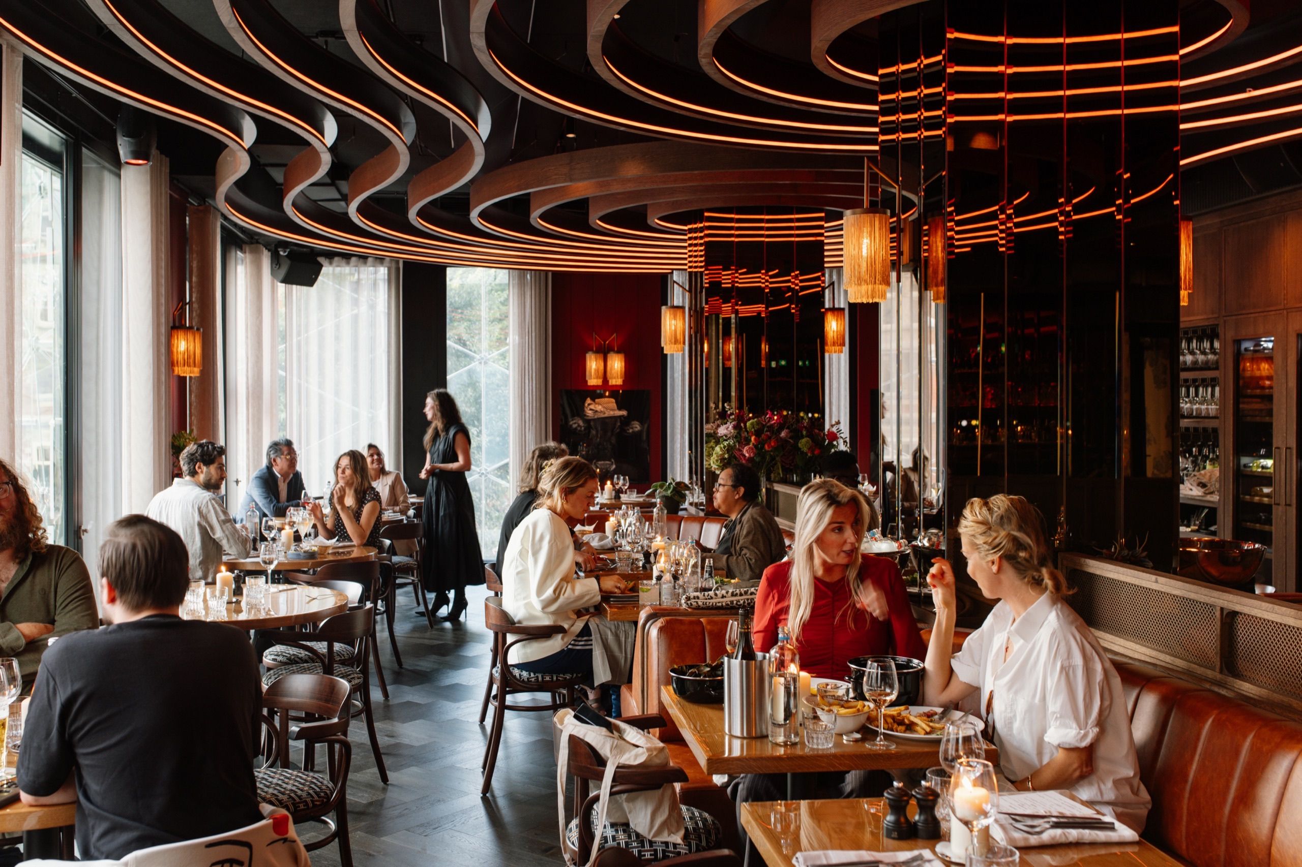 Gasten aan tafel in de Bistro bij daglicht, met leren banken en hoge ramen op het Leidseplein