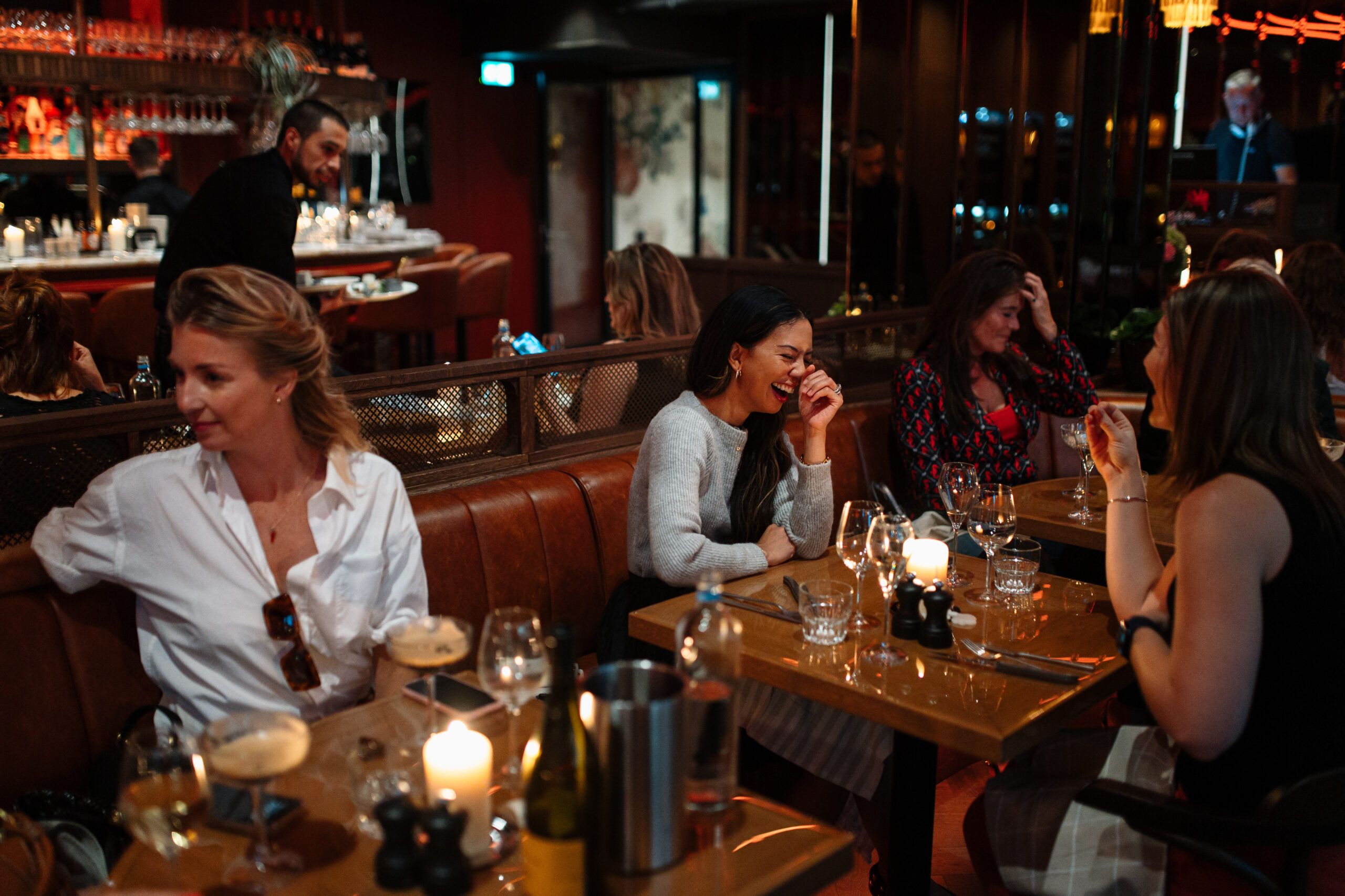 Friends laughing together at a candlelit table in a leather booth
