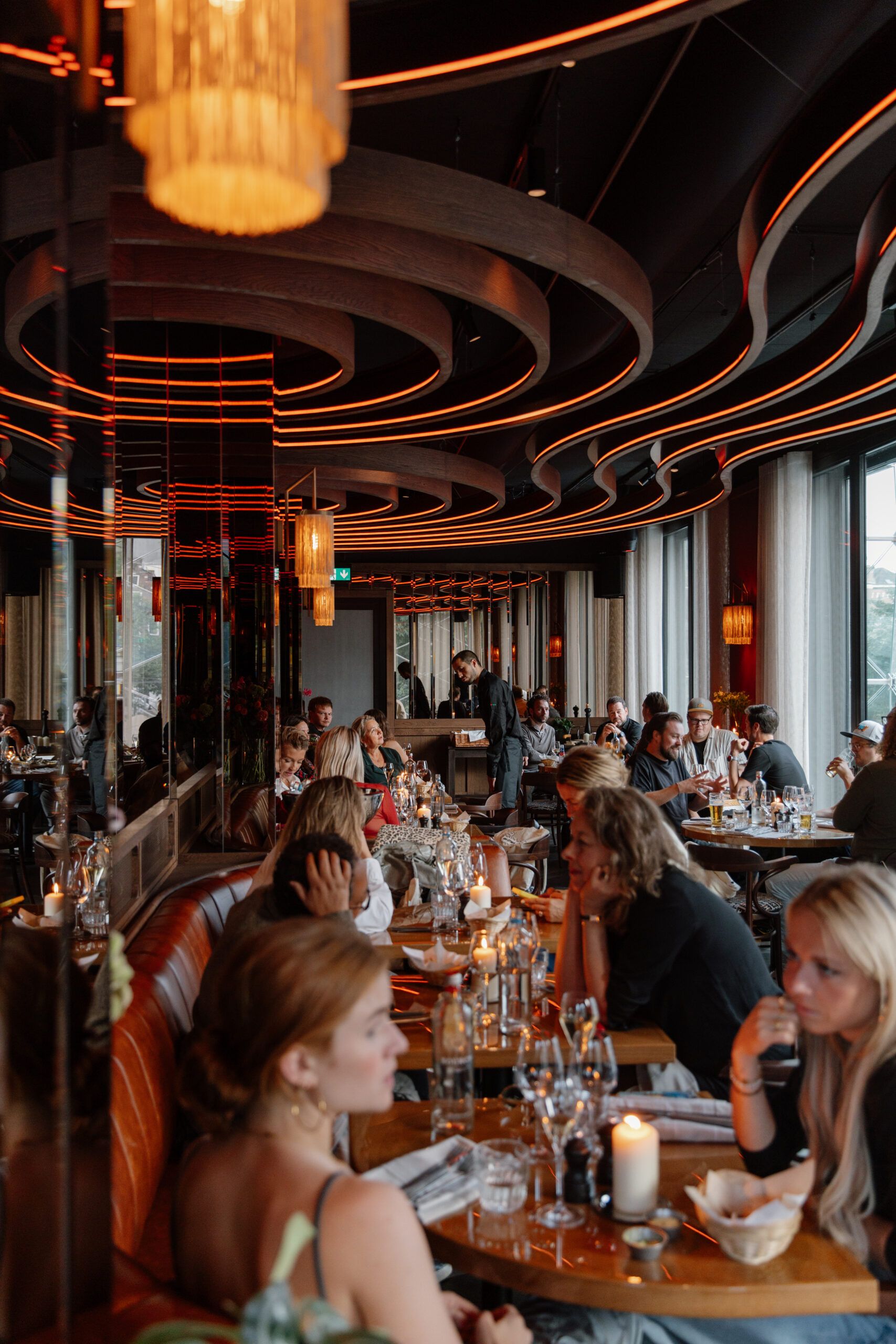 Guests dining in the Bistro under the curved, lit ceiling bands, with candles on the tables