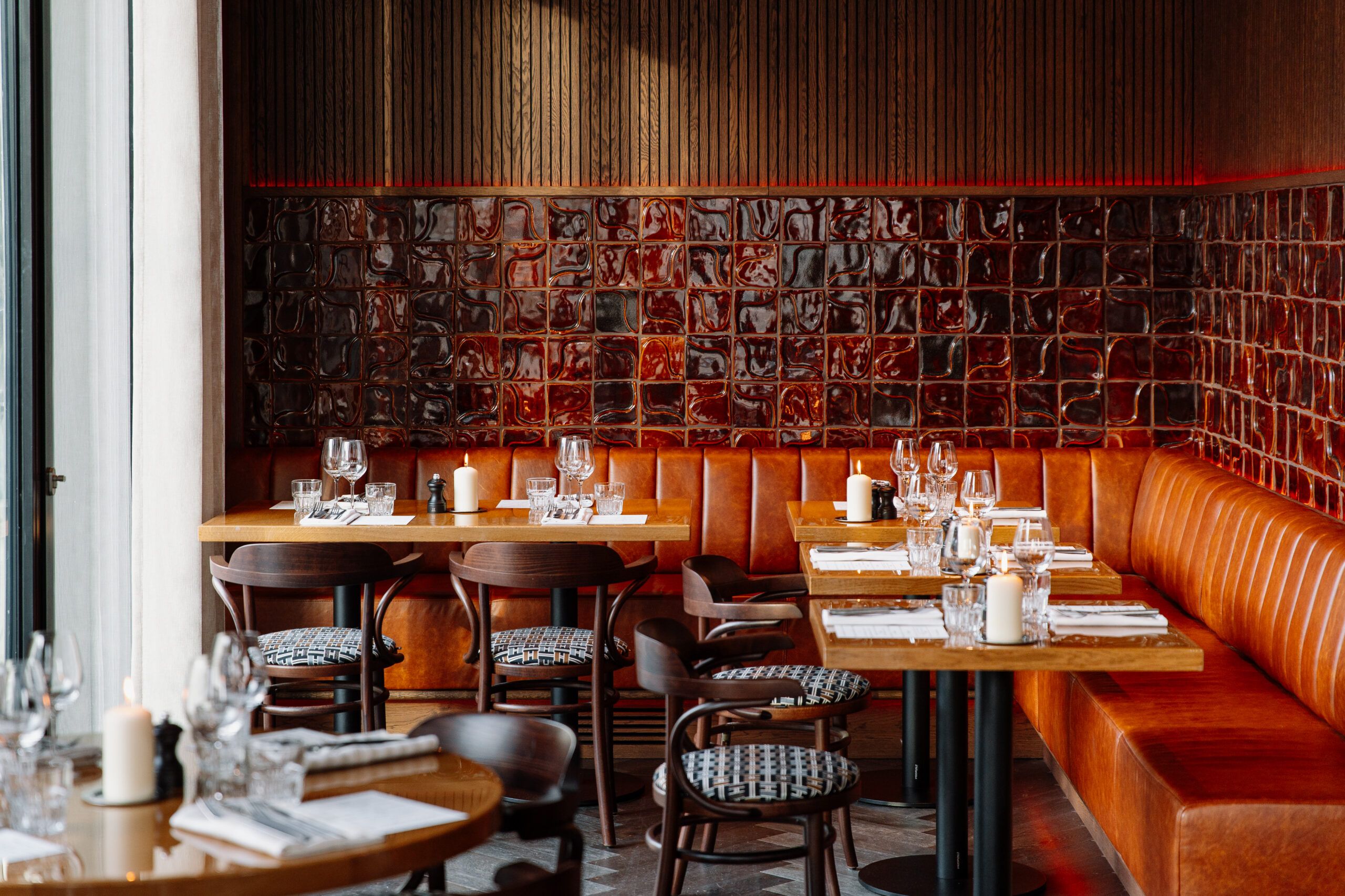 Laid tables along an orange leather banquette against a wall of dark red tiles