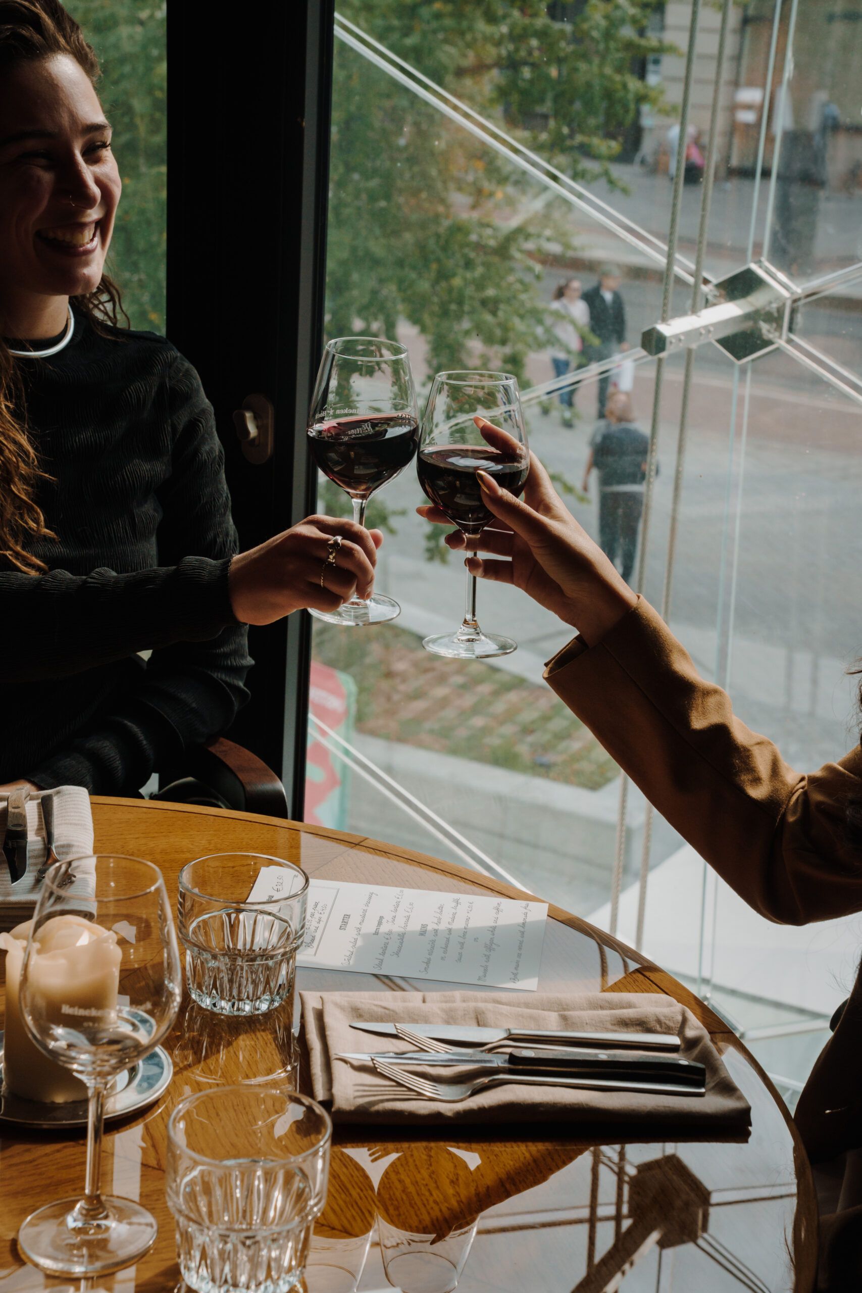 Two guests toasting with red wine at a table by the window