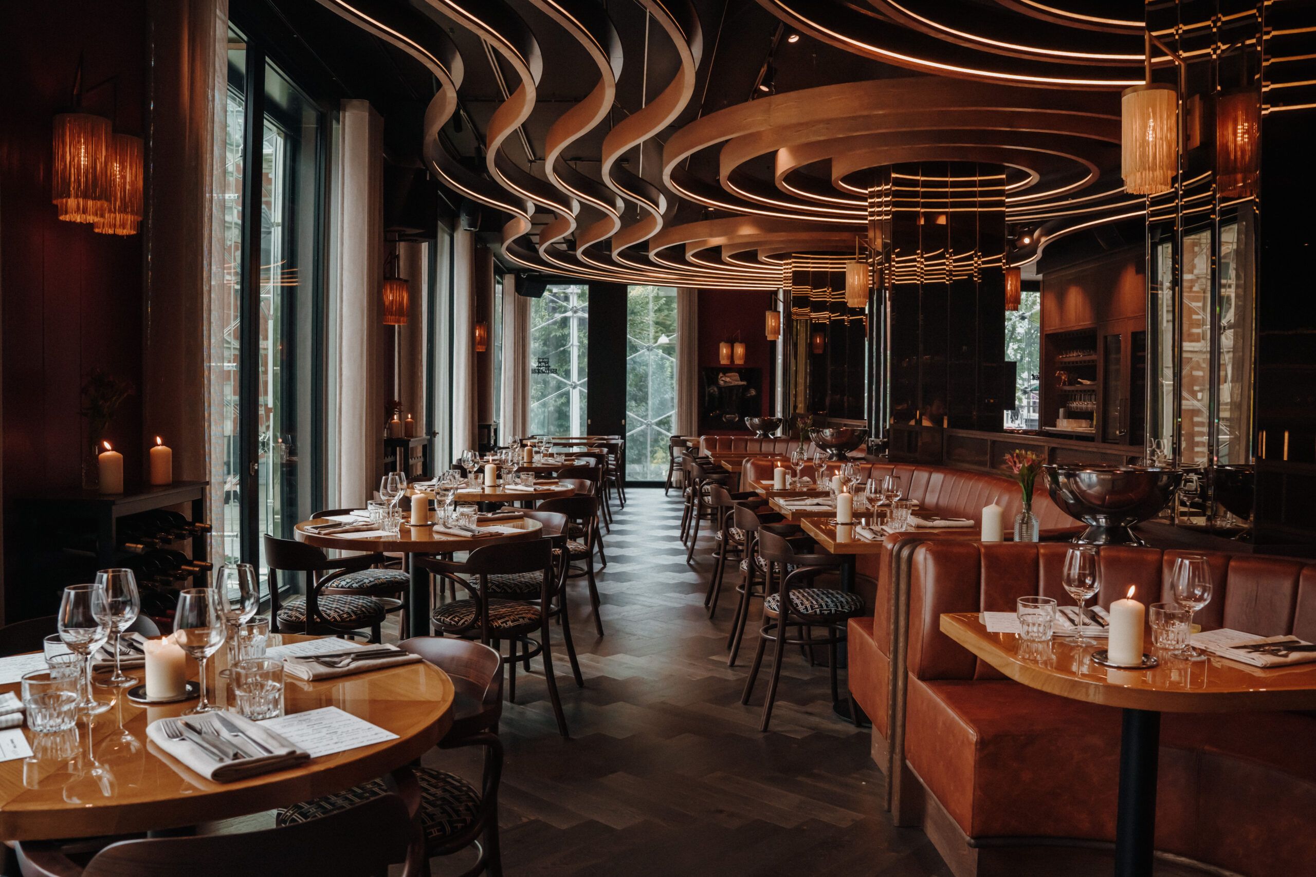 The Bistro dining room with set tables, leather banquettes, candles and curved lit ceiling bands