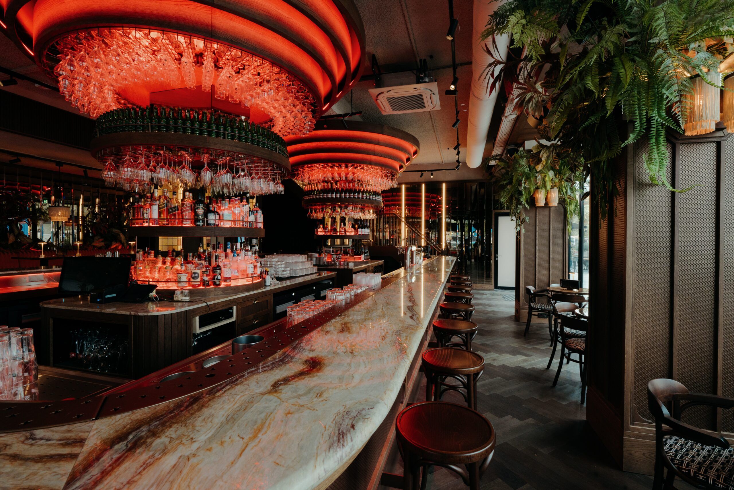 The Grand Café bar with its long marble counter, wooden bar stools and round glass racks lit in red