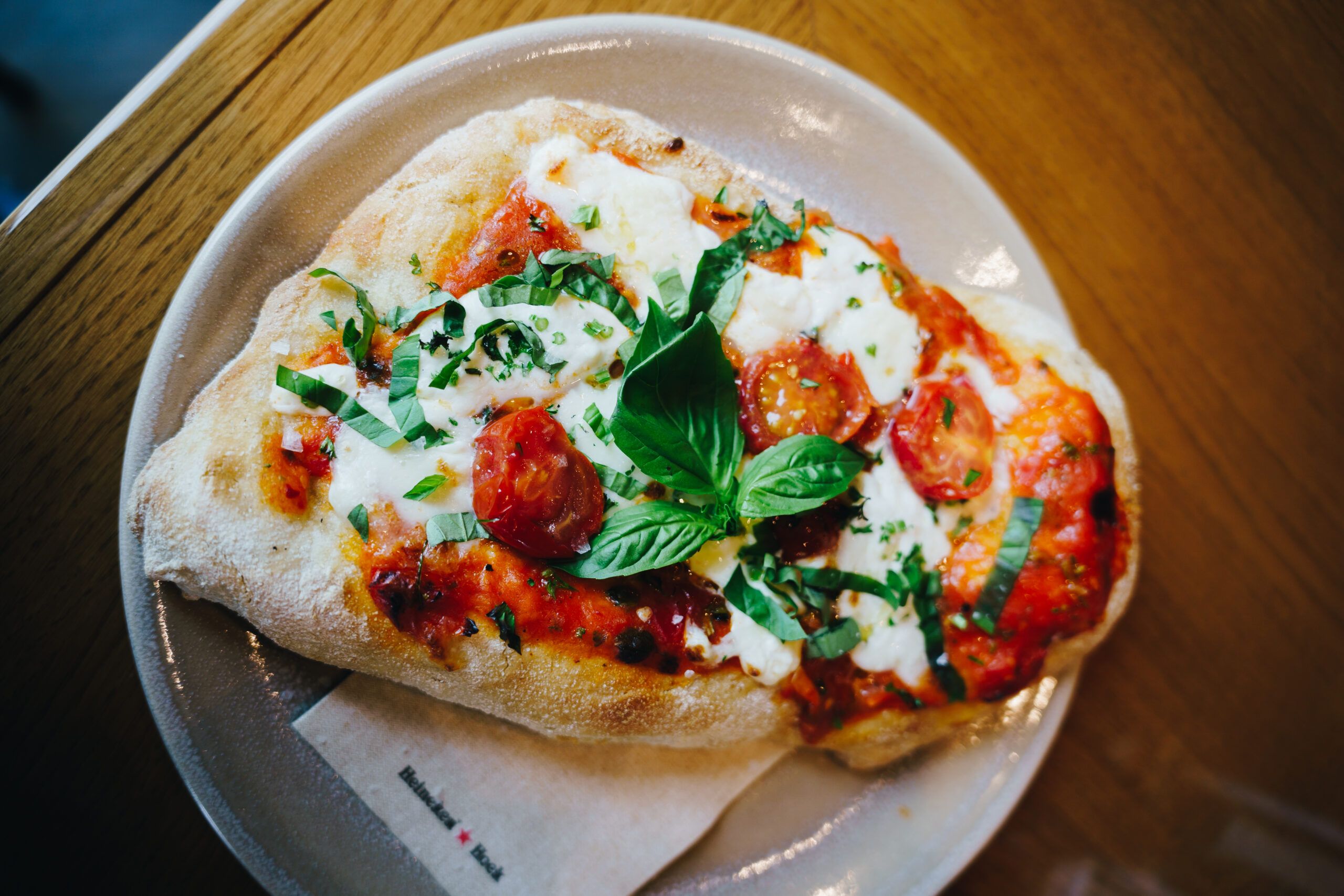A flatbread pizza with tomato, mozzarella, roasted cherry tomatoes and fresh basil on a wooden table
