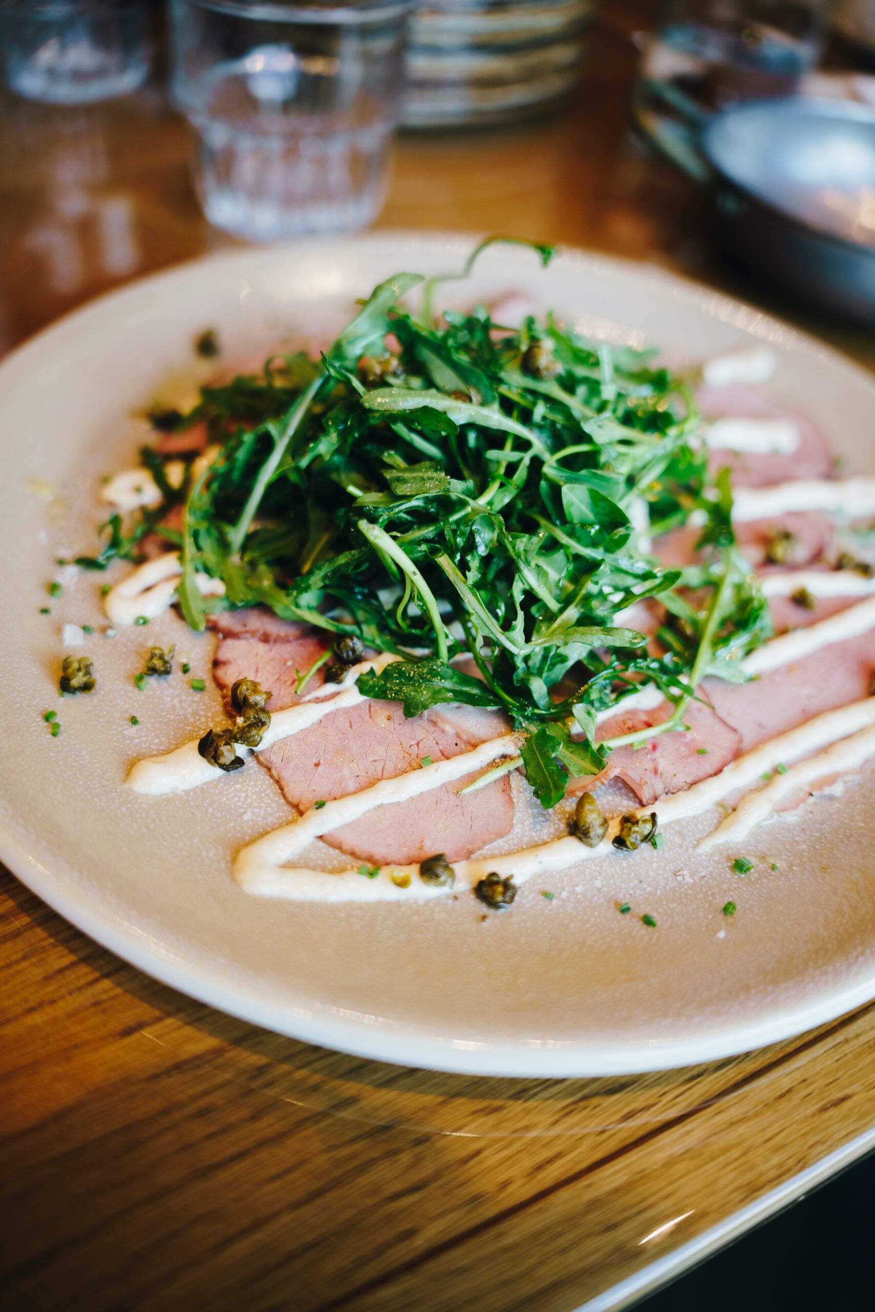Thinly sliced meat with a creamy sauce, rocket and crispy capers on a light plate