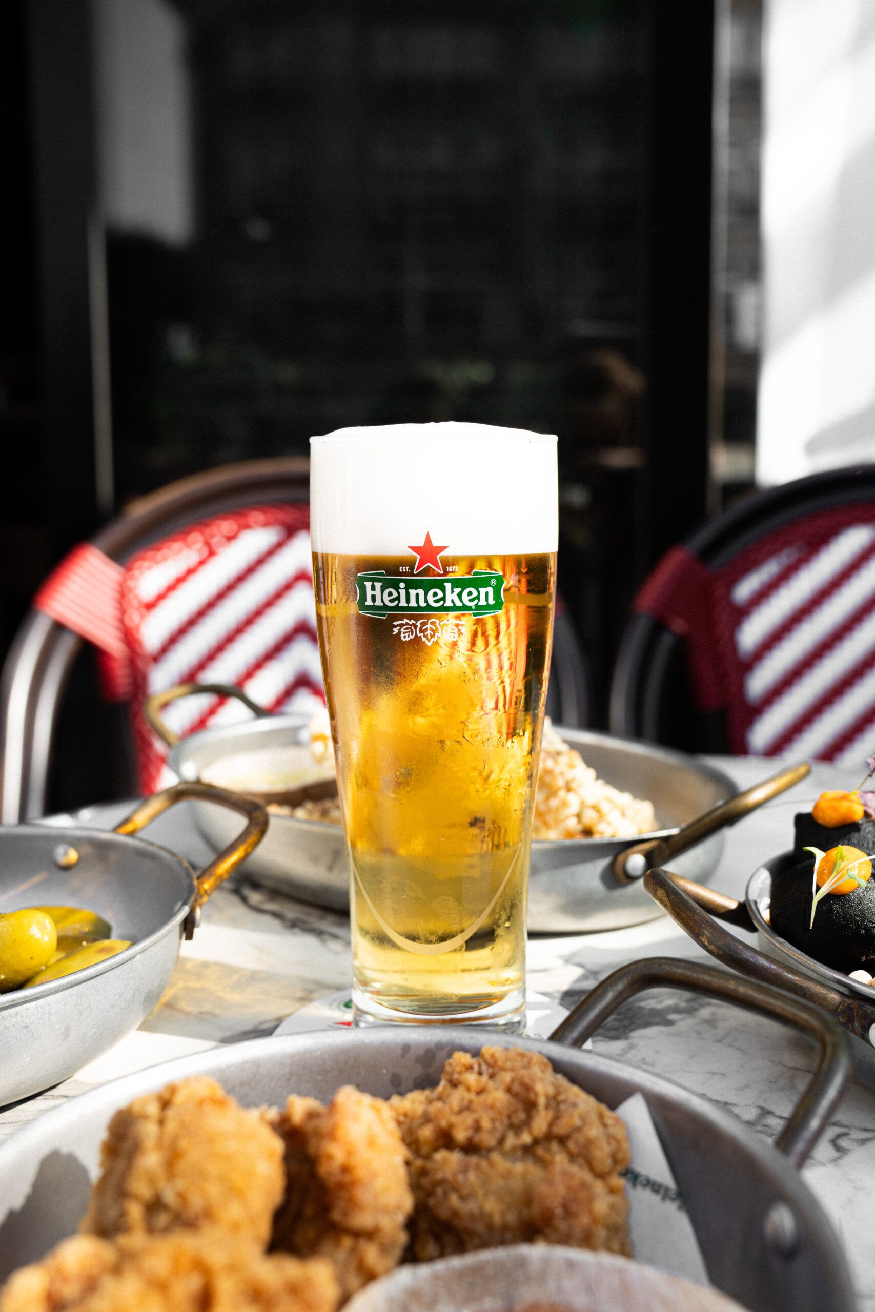 A glass of Heineken on a marble table among bar snacks: fried chicken, olives and croquettes